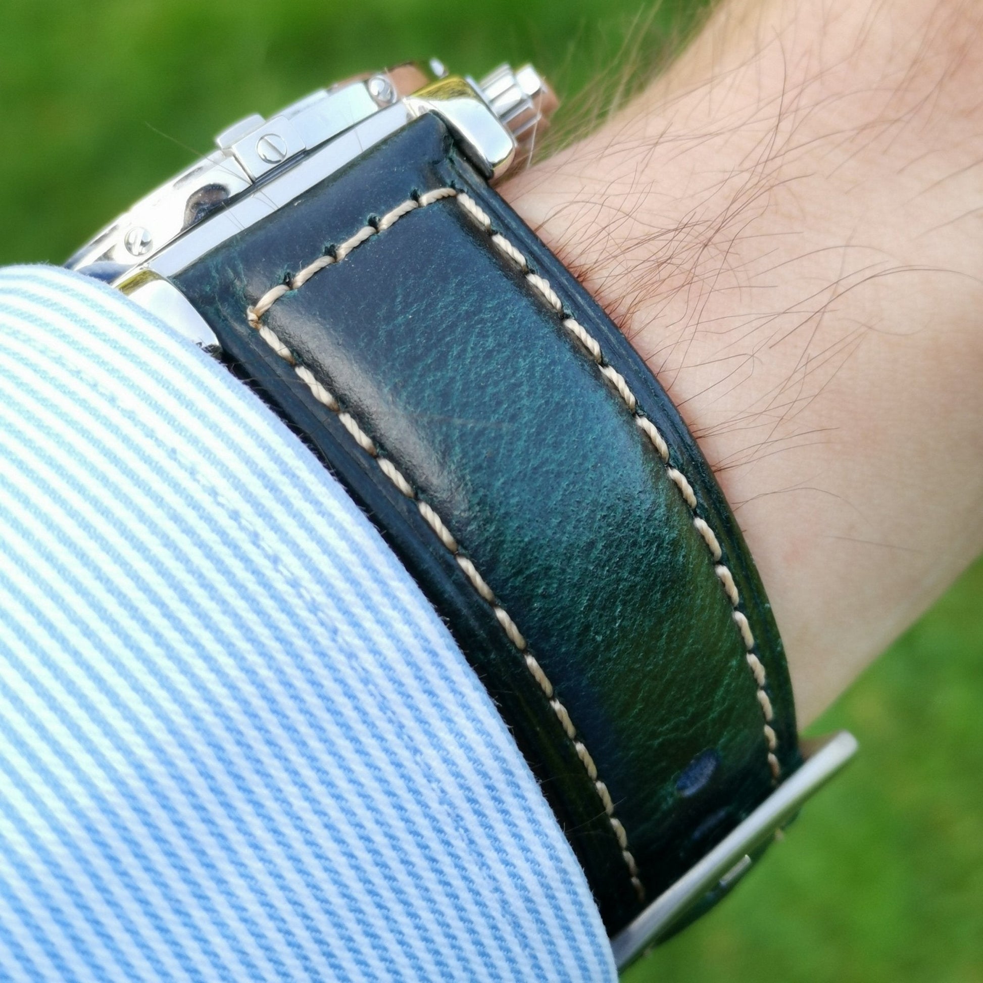 Wrist shot of the Berlin blue full grain leather watch strap. Strap on a males wrist with a shirt sleeve. Grass background.